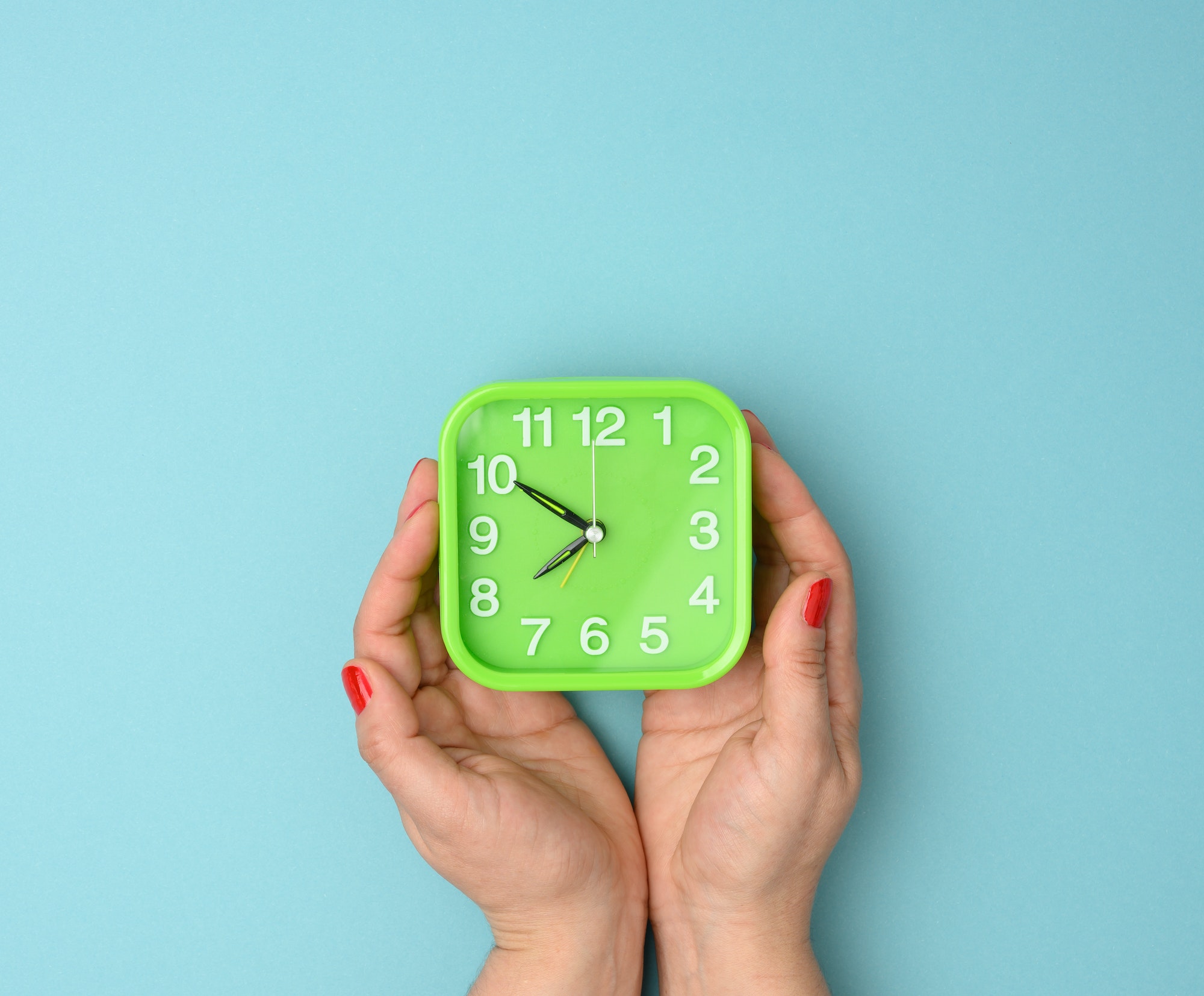 Woman's hand holds a green square alarm clock, time is ten to eight in the morning